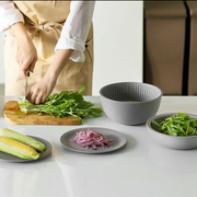 A food preparation scene with a person chopping greens, showing the versatile Like-it bowls and plates used for holding ingredients.