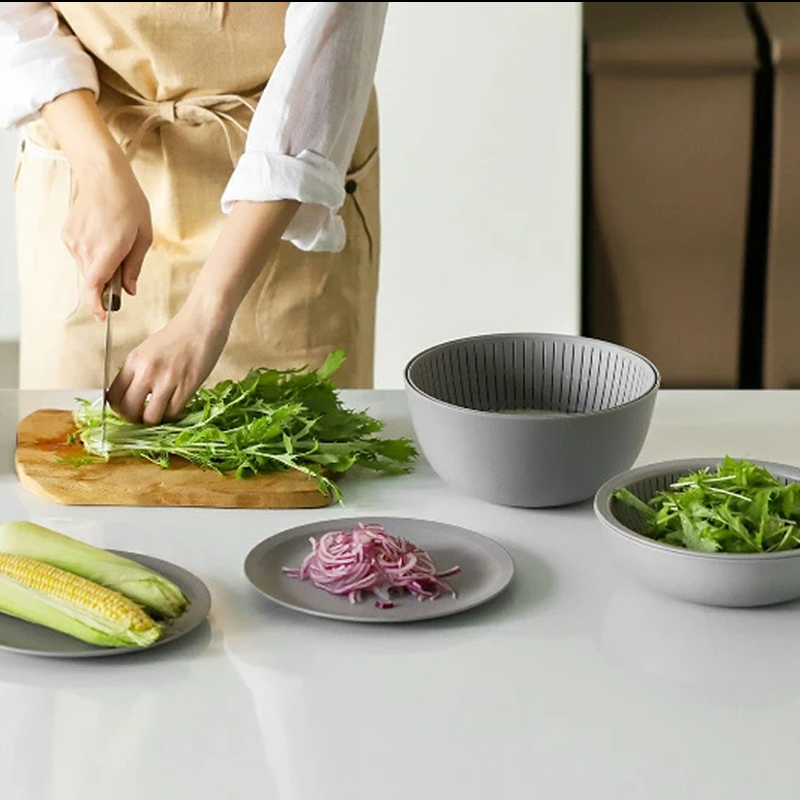 A food preparation scene with a person chopping greens, showing the versatile Like-it bowls and plates used for holding ingredients.