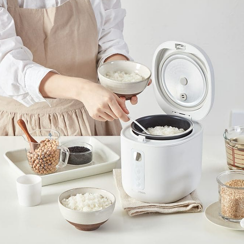 A woman serving freshly cooked rice from the LocknLock Macaron Mini Rice Cooker, demonstrating its ease of use and efficiency in a home kitchen setting.
