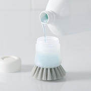 Pouring detergent into the Marna Antibacterial Dispenser Brush - A bottle of dishwashing soap being poured into the refillable chamber of the Marna brush.
