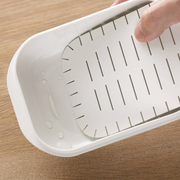 A close-up view of the removable slatted inner tray being placed inside the Marna Kiwami Freeze & Microwave Rice Container.