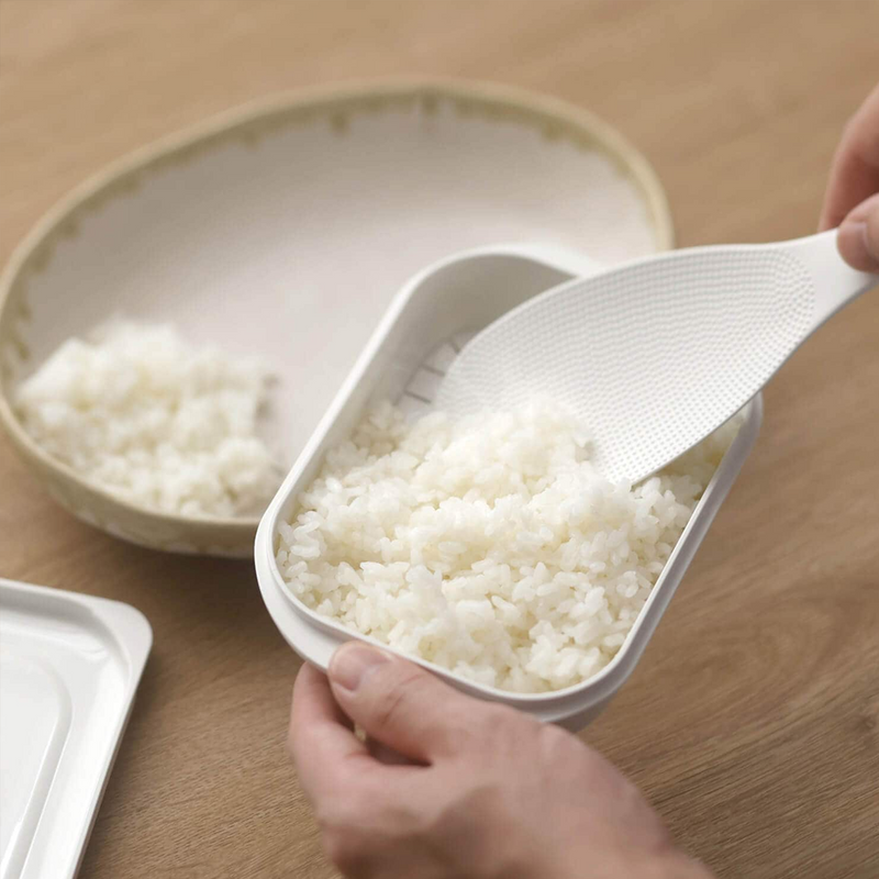 Serving freshly heated rice from the Marna Kiwami Freeze & Microwave Rice Container with a white rice paddle.