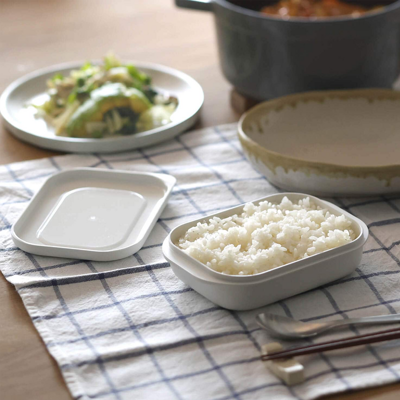 The Marna Kiwami Freeze & Microwave Rice Container filled with cooked rice, displayed as part of a meal setting on a checked tablecloth.