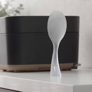  Marna Premium TPX Standing Rice Scoop placed beside a rice cooker and ceramic bowls.