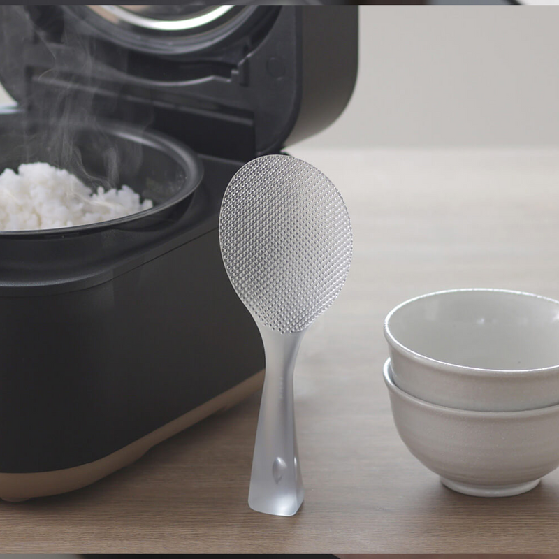 Marna Premium TPX Standing Rice Scoop placed on a white surface next to a rice cooker.