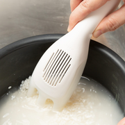 A person using the white Marna rice washer to stir rice and cloudy starch water in a rice cooker pot.
