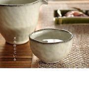 A lifestyle photo of the Midnight Elegance Kohiki Sake Cup filled with sake, presented on a placemat with a pitcher in the background.