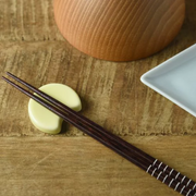 Oda Pottery Mount Fuji Moon Chopstick Rest in pale yellow, shaped as a half-circle to cradle a pair of dark wood chopsticks, styled on a wooden surface alongside a white ceramic plate
