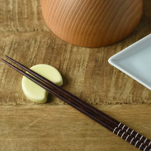 Oda Pottery Mount Fuji Moon Chopstick Rest in pale yellow, shaped as a half-circle to cradle a pair of dark wood chopsticks, styled on a wooden surface alongside a white ceramic plate
