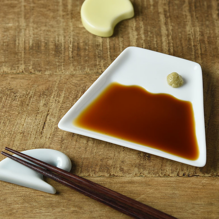 Mino Yaki Mount Fuji Soy Sauce Plate with soy sauce and a small dab of wasabi, accompanied by chopsticks on a wooden table.