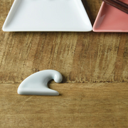Oda Pottery Mount Fuji Wave Chopstick Rest in light blue porcelain, sculpted in the shape of a cresting wave, styled on a wooden surface alongside white and pink ceramic plates