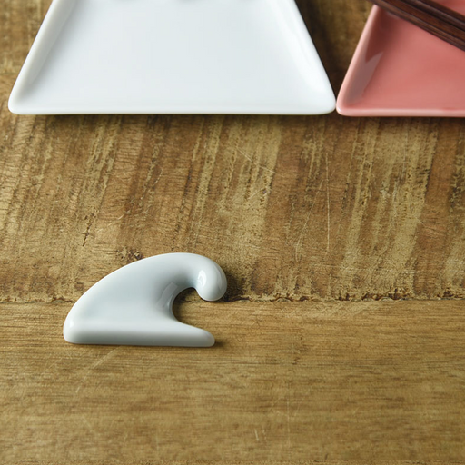 Oda Pottery Mount Fuji Wave Chopstick Rest in light blue porcelain, sculpted in the shape of a cresting wave, styled on a wooden surface alongside white and pink ceramic plates