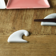 Oda Pottery Mount Fuji Wave Chopstick Rest in white porcelain, sculpted in the shape of a cresting wave, styled on a wooden surface alongside a pink ceramic plate and dark wood chopsticks