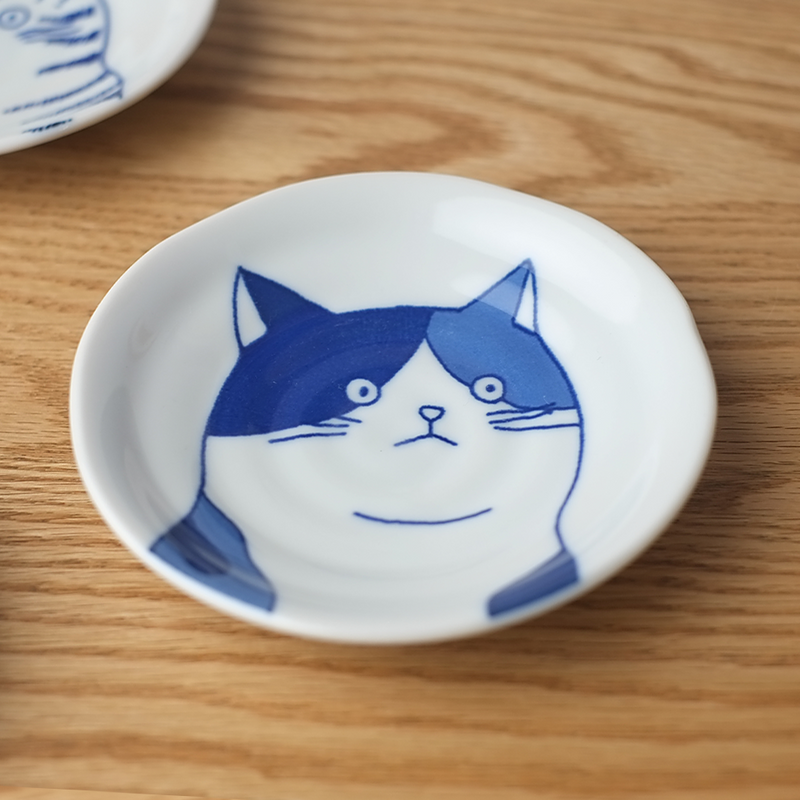 Small white dish with blue cat illustration on a wooden surface