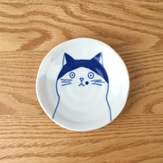 A top-down view of the Shichita Mino Yaki Cat Nora side plate, showing the wide-eyed, contemplative cat illustration on a white porcelain surface.