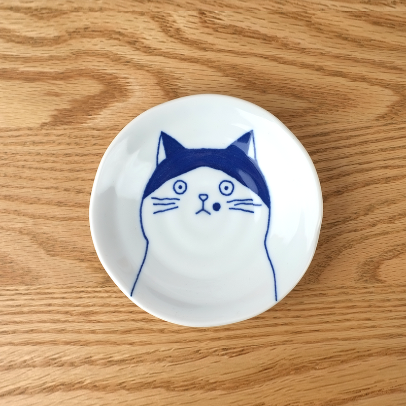 A top-down view of the Shichita Mino Yaki Cat Nora side plate, showing the wide-eyed, contemplative cat illustration on a white porcelain surface.