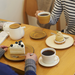 A cozy setting where two people enjoy tea and desserts, featuring a Miyama Bico Series teapot with a mustard lid, and various cakes on a wooden table.