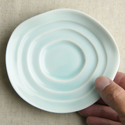 A hand holding the Miyama Haas Soy Sauce Plate, displaying its concentric ripple design and pale green celadon glaze.

