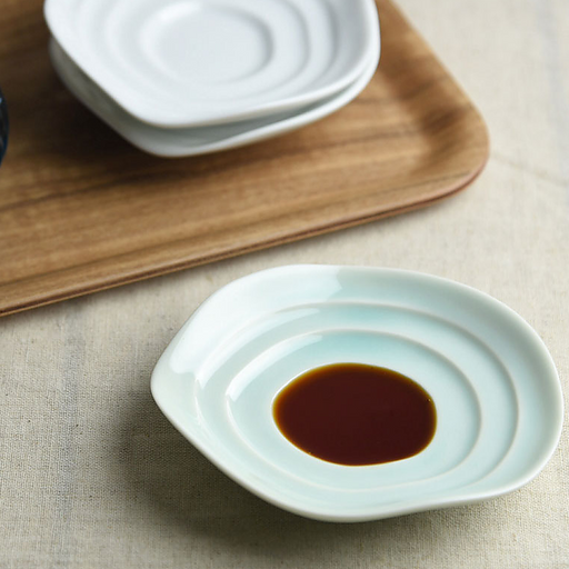 The Miyama Haas Soy Sauce Plate shown in use, holding a pool of soy sauce that highlights the plate's unique rippled shape.