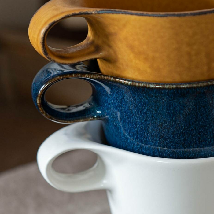 Close-up view of stacked Miyama Bico Series stoneware mugs in mustard, blue, and white, highlighting their compatibility for stacking and the smooth, colorful glazes.