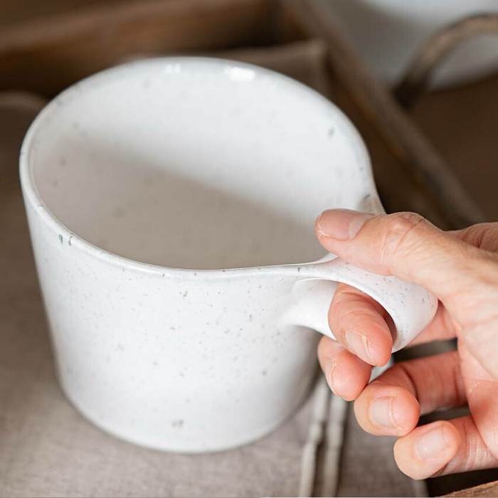 Close-up of a hand holding a Miyama Bico Series white speckled stoneware mug, focusing on the ergonomic handle and the mug's textured surface.