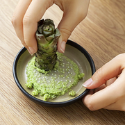 Grating fresh wasabi root on a ceramic Japanese grater with sharp ridges.

