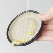 A piece of ginger on a ceramic grater surrounded by freshly grated ginger, next to a Japanese meal setting.

