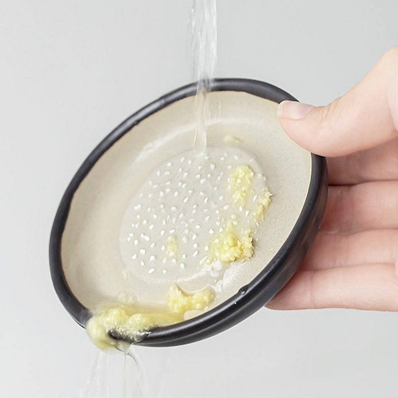 A piece of ginger on a ceramic grater surrounded by freshly grated ginger, next to a Japanese meal setting.

