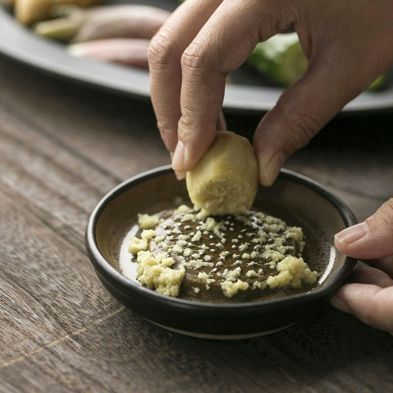 Hand dipping a piece of bread into a bowl of pesto on a wooden table