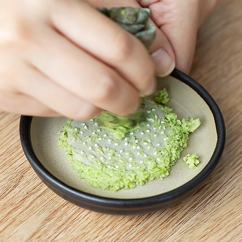 Hand grating fresh wasabi using a Japanese ceramic grater with fine ridges.


