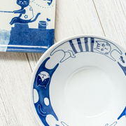 A close-up of the cat illustrations on the rim of the Nekomaruke donburi bowl, placed on a white wooden surface.
