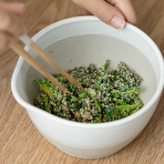 White bowl with green salad and sesame seeds on a wooden table