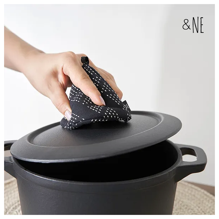 A person's hand lifting a heavy pot lid using the black &NE pot holder with white dotted embroidery.