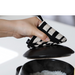 A hand using a &NE pot holder with a black and white geometric design to stir rice in a black ceramic pot, highlighting its functionality in kitchen use.