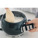 Close-up of a hand lifting a black pot lid using a &NE pot holder, featuring a black and white geometric pattern, demonstrating the pot holder's heat resistance and grip.