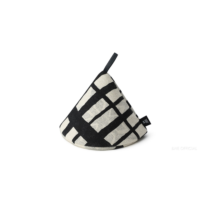 A black and white geometric patterned &NE pot holder hanging on a silver hook against a white brick wall, showcasing its practical and decorative design.