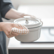 A person using the striped beige pot holder to grip the side handle of a hot enamel pot.
