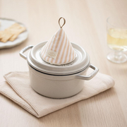 The beige striped cone pot holder sitting decoratively on top of a pot lid, adding a charming accent to the kitchen.