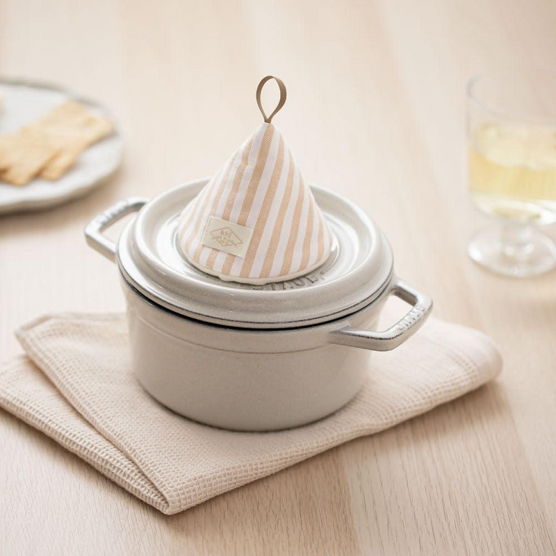The beige striped cone pot holder sitting decoratively on top of a pot lid, adding a charming accent to the kitchen.