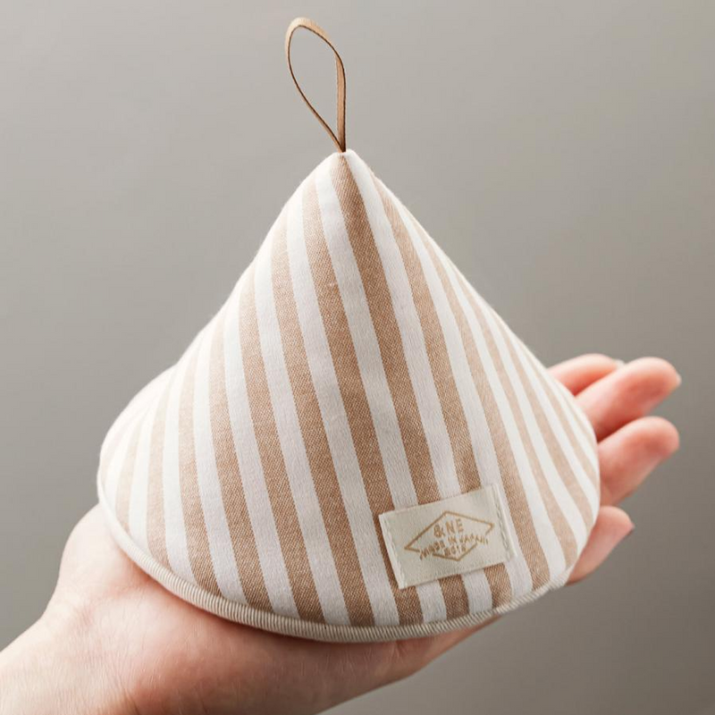 A close-up of a cone-shaped Japanese pot holder with beige and white stripes, held in a hand to show its size and leather hanging loop.