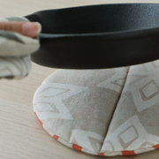 Close-up of a pot being placed on a neutral-toned round pot holder on a light wooden table.

