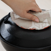 Hand gripping the lid of a donabe pot using the reverse side of the patterned pot holder.