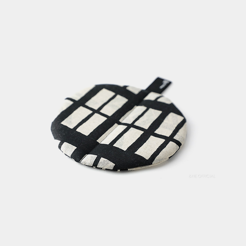 The &NE Manmaru Pot Holder and Table Mat, a round, flat fabric trivet with a modern black and white pattern.
