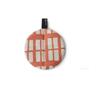 Top view of a coral-patterned round pot holder with a centred hanging tag.

