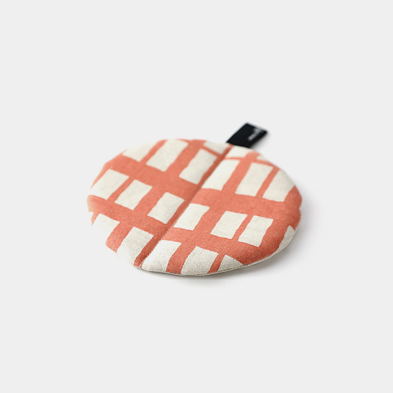 The &NE Manmaru Pot Holder and Table Mat, a round, flat fabric trivet with a modern coral and white pattern.

