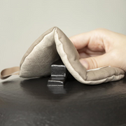 A hand using the folded beige Manmaru pot holder to safely grip the hot handle of a black cast iron pot lid.