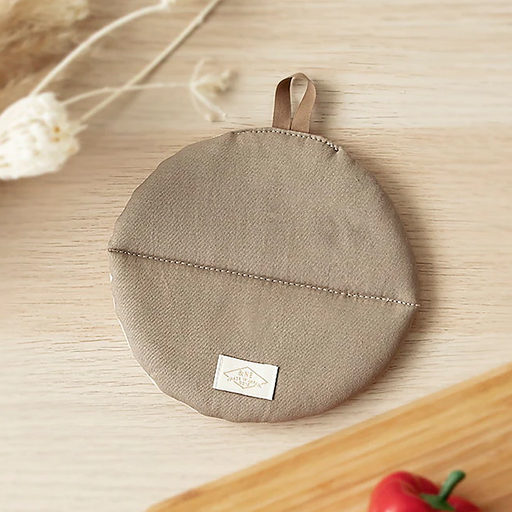 A flat lay of the round &NE Manmaru Pot Holder in Natural Beige, showing the central stitching line, logo tag, and hanging loop.