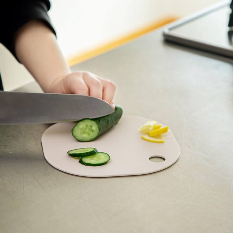 &NE Nikii Mini Antibacterial Cutting Board in a beige colour, featuring a compact hybrid shape (round and square) being used to slice cucumber.