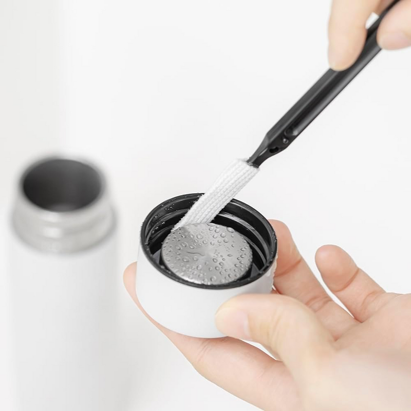 A person using the &NE Nikii mini cleaning brush to clean the internal threads of a drink bottle lid.
