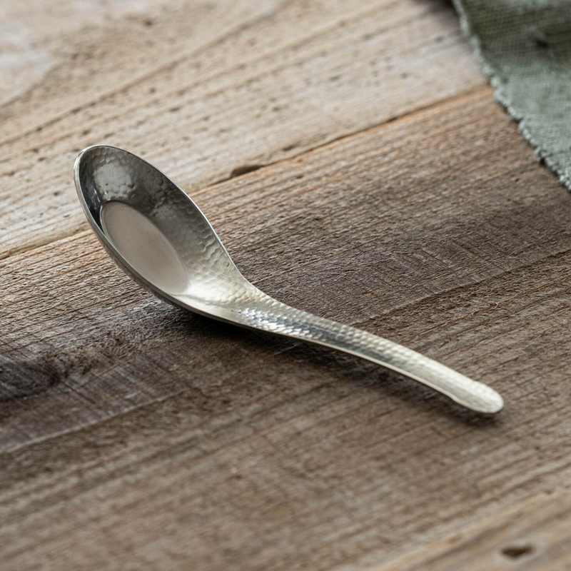 Nagomi Hammered Style stainless steel ramen spoon with tsuchime texture and deep rounded bowl, shown on a weathered wooden surface